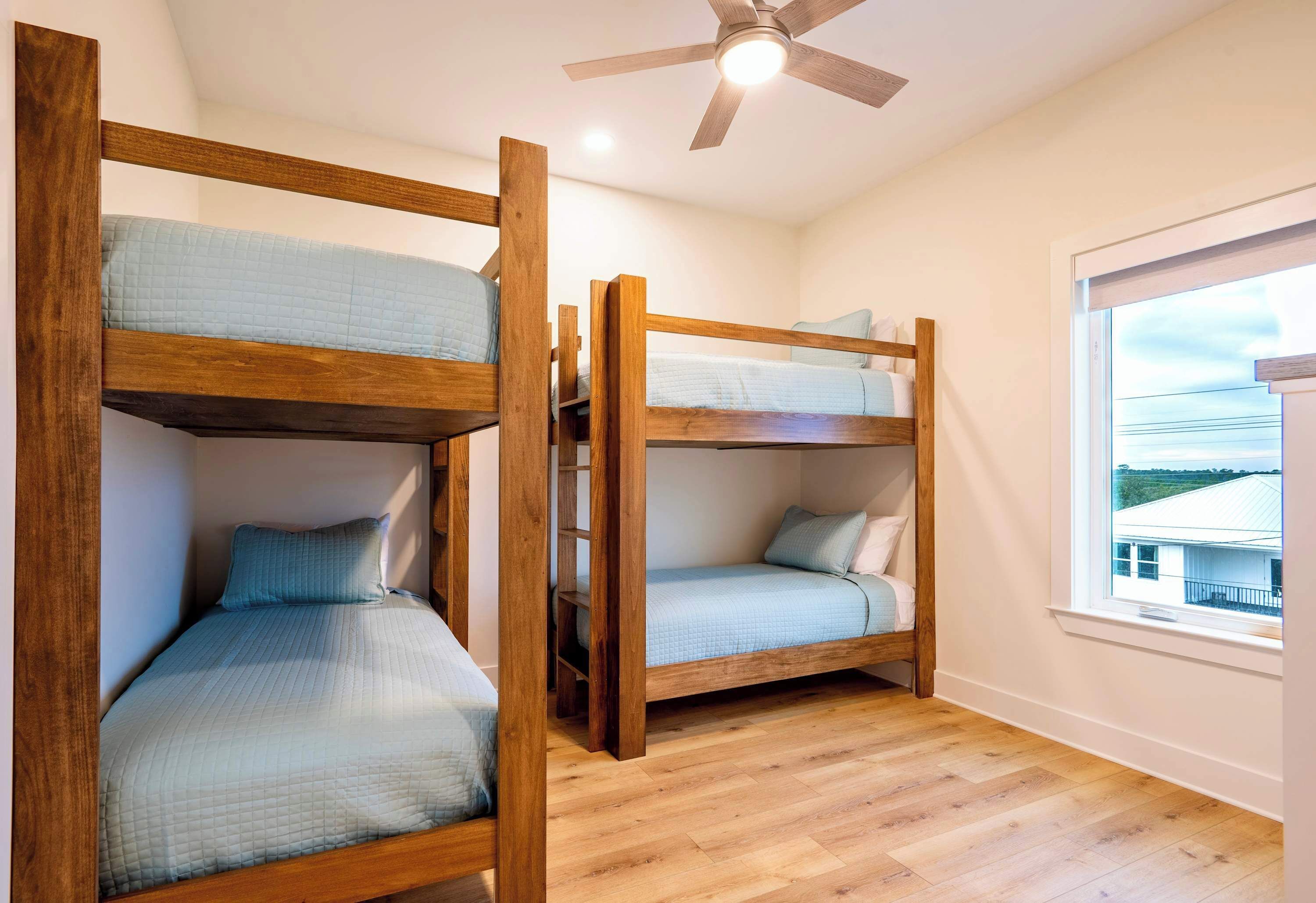 A room with two bunk beds, a ceiling fan, and a window with a view.