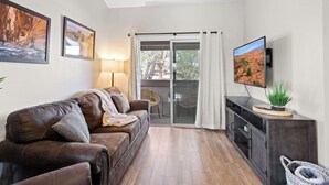 Een woonkamer met een leren bank, een flatscreen-tv, een schuifdeur naar een buitenruimte en een kast met een plant erbovenop.