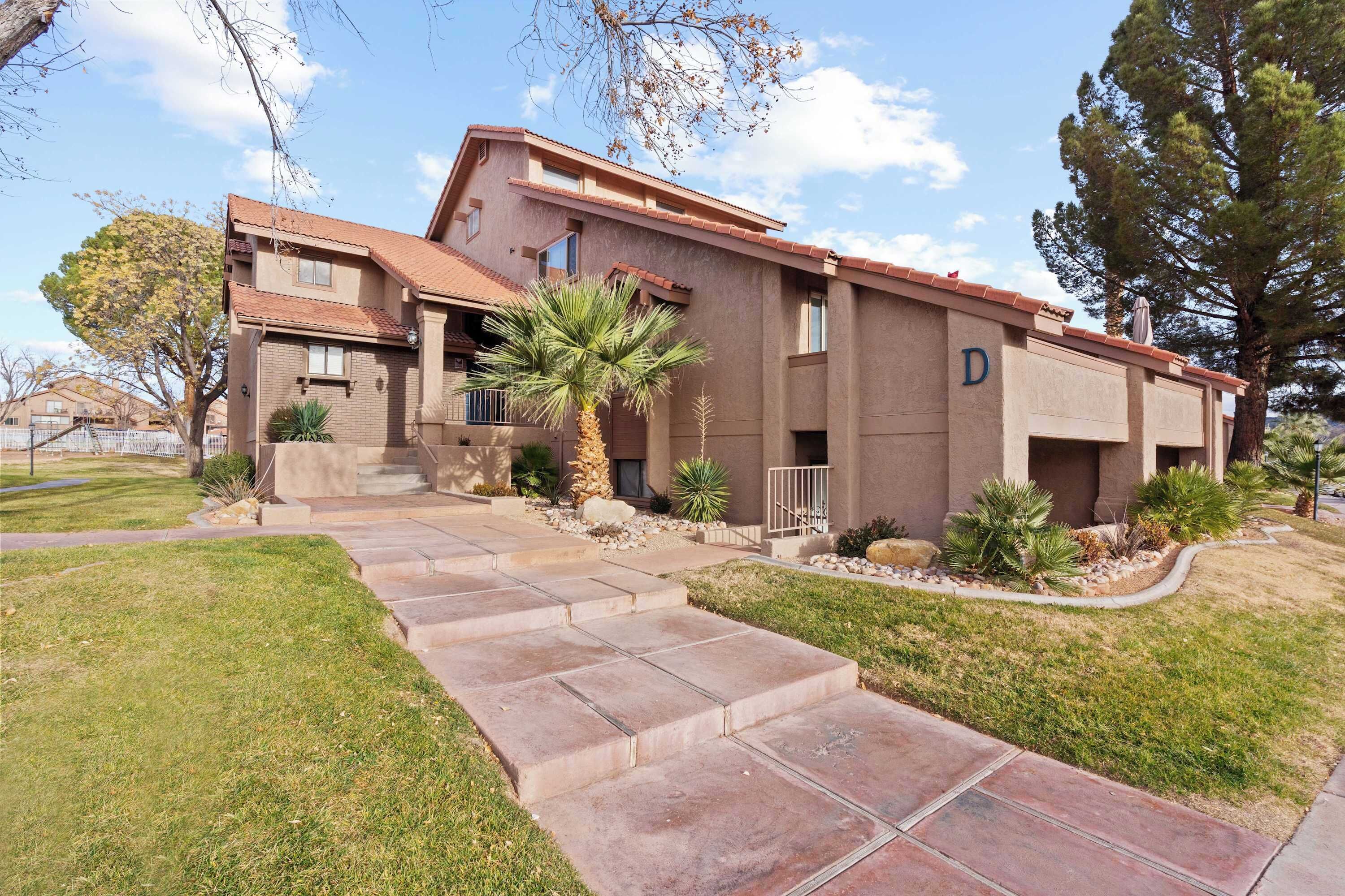 A two-story house with a stone pathway leading to the entrance, surrounded by well-maintained grass and small plants.
