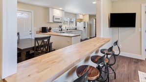 A modern kitchen with white cabinets, a wooden countertop, and a built-in microwave. There is a dining area with a wooden table and chairs. A flat-screen TV is mounted on the wall. - Diana's Place (Murfreesboro)