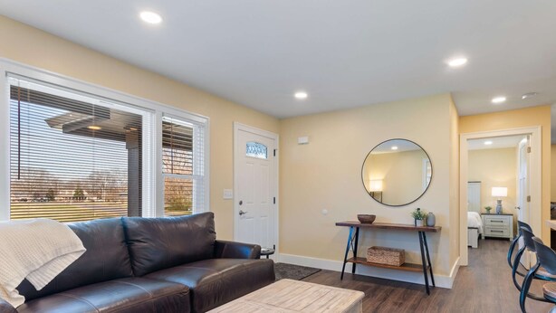 A living room with a brown leather couch, a wooden coffee table, a round mirror, and a dining area with chairs and a table. - Diana's Place (Murfreesboro)