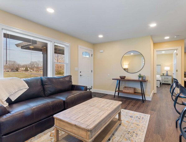 A living room with a brown leather couch, a wooden coffee table, a round mirror, and a dining area with chairs and a table.