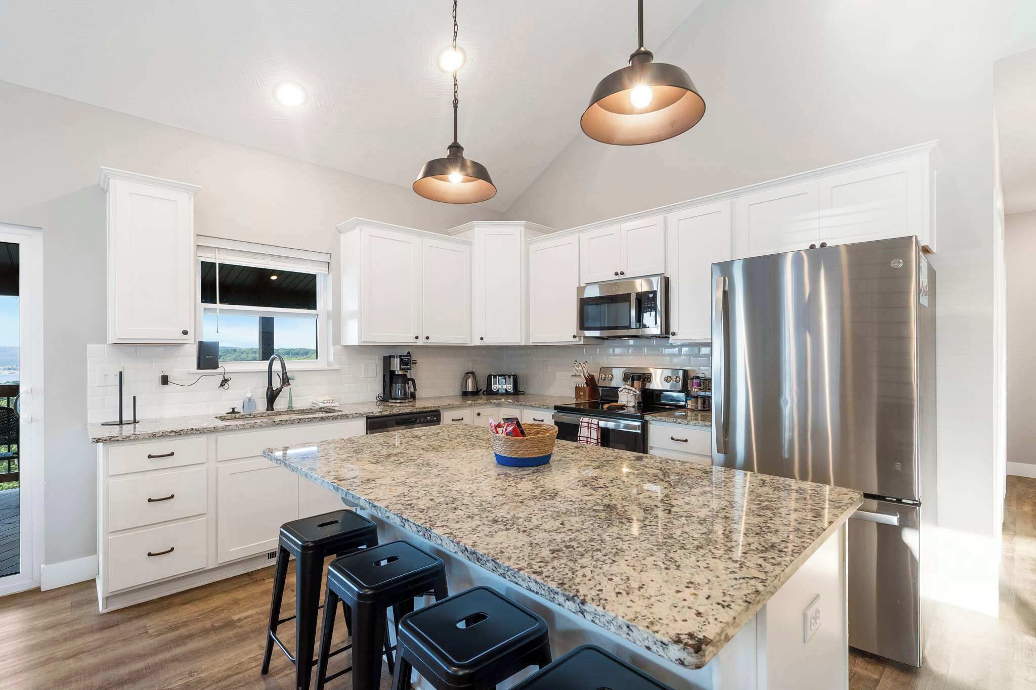 A modern kitchen with white cabinets, stainless steel appliances, a granite countertop, and pendant lighting.