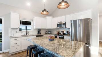A modern kitchen with white cabinets, stainless steel appliances, a granite countertop, and pendant lighting.