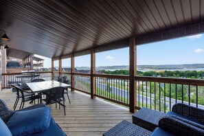 A covered outdoor deck with a table and chairs, a grill, and a view of a road and landscape. - A Birds Eye Bridge View - 5 BDR w/ Private Hot Tub (Kimberling City)