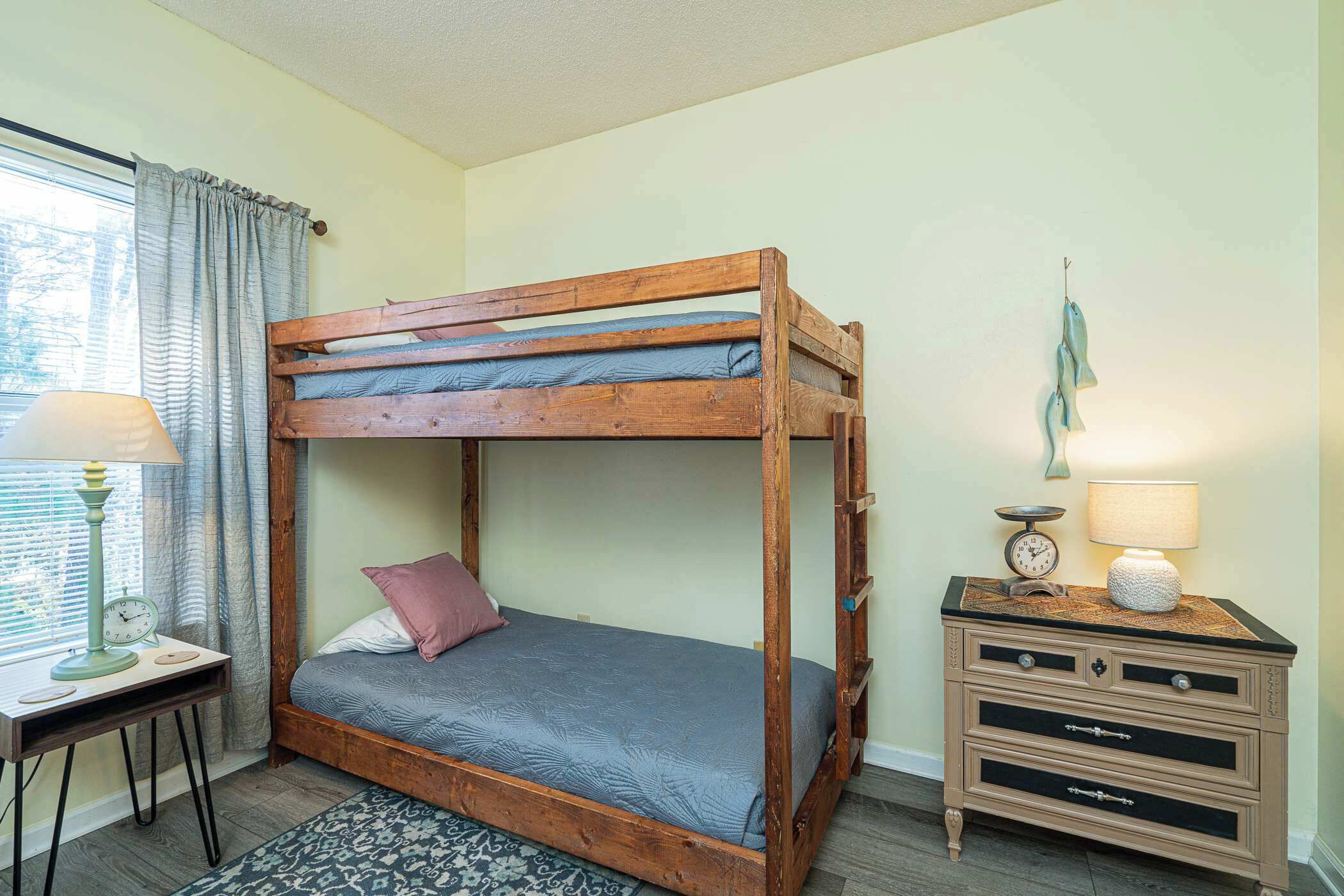 Una cama litera con estructura de madera, una mesita de noche con lámpara, y un aparador con cajones.