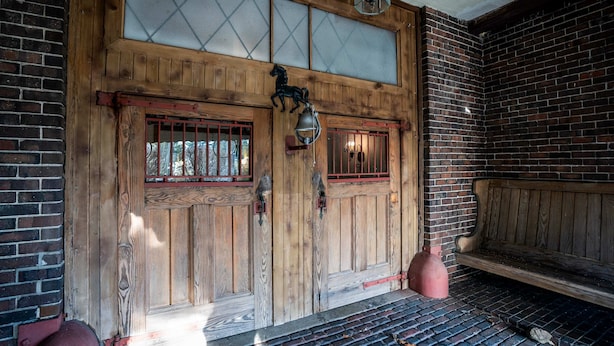 Una porta in legno con pannelli di vetro, una decorazione a cavallo e una panca all'interno di un edificio con pareti in mattoni.