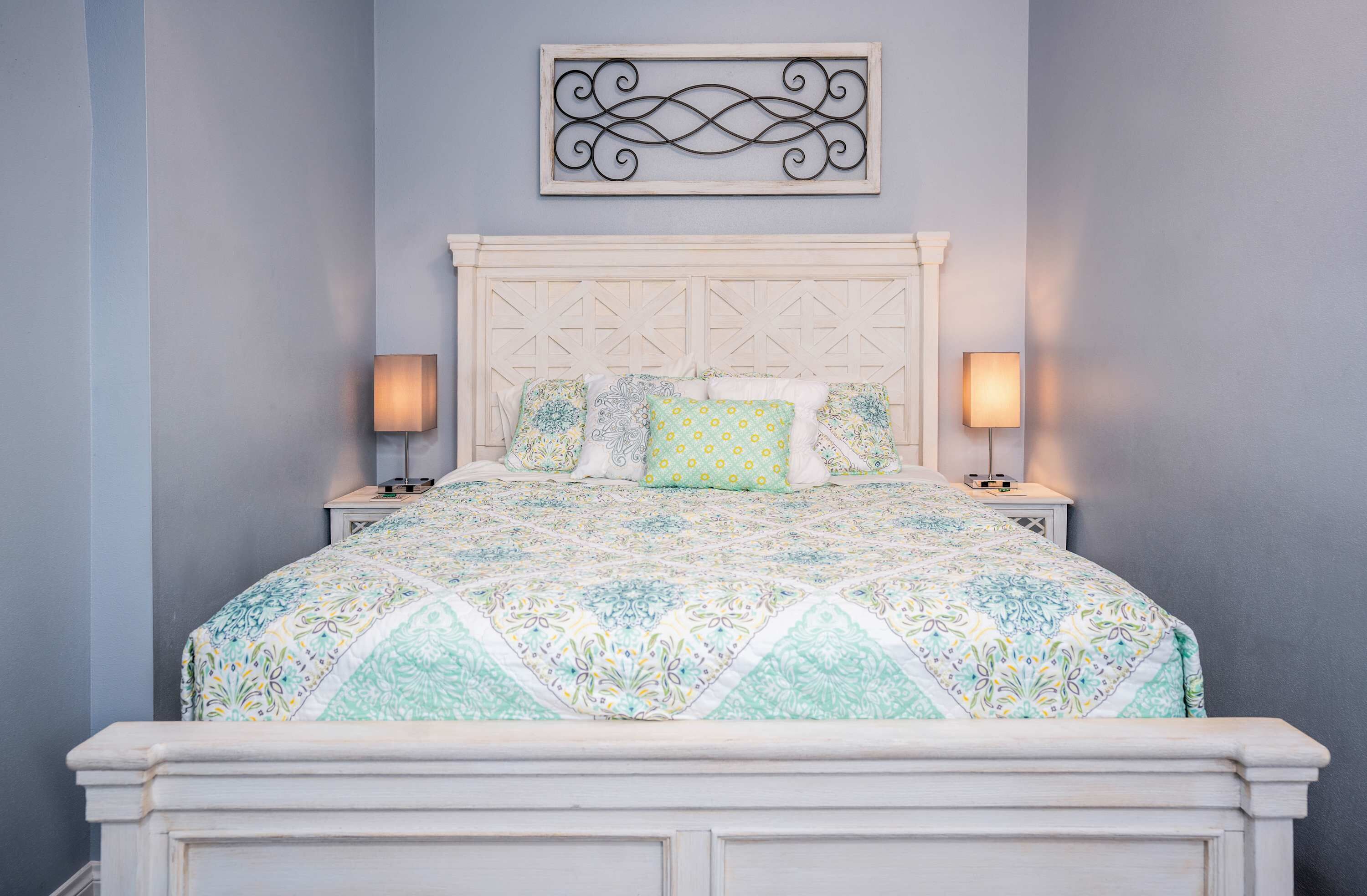 Una cama con un edredón estampado, dos lámparas de noche y un adorno decorativo sobre la cama.