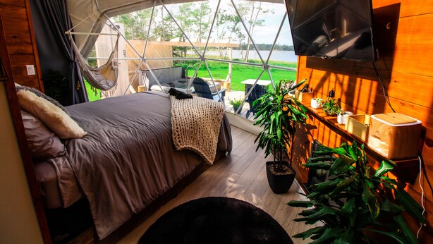 Alojamiento con tienda de campaña, cama, televisión y vista a un campo verde.
