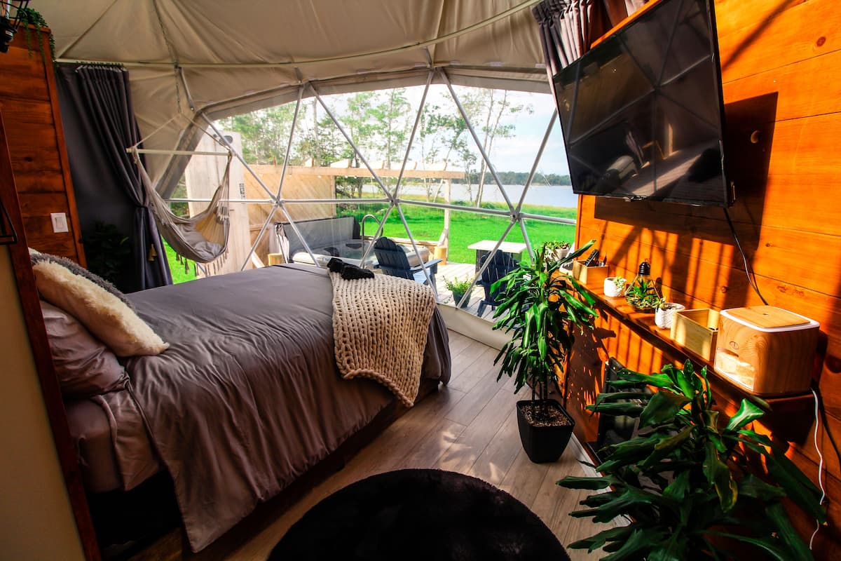 A tented accommodation with a bed, a TV, and a view of a green field.