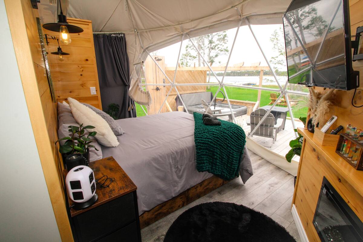 A tented accommodation with a bed, a TV, and a view of the outdoors.