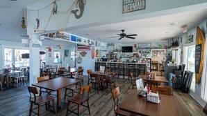 A restaurant with wooden tables and chairs, a kitchen area, and various decorations including a mermaid sign. - The Turtle Nest Resort Condo w/ Pool! (Panama City Beach)