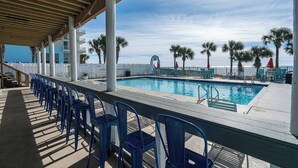 A poolside area with blue chairs, a pool, palm trees, and a view of the ocean. - The Turtle Nest Resort Condo w/ Pool! (Panama City Beach)