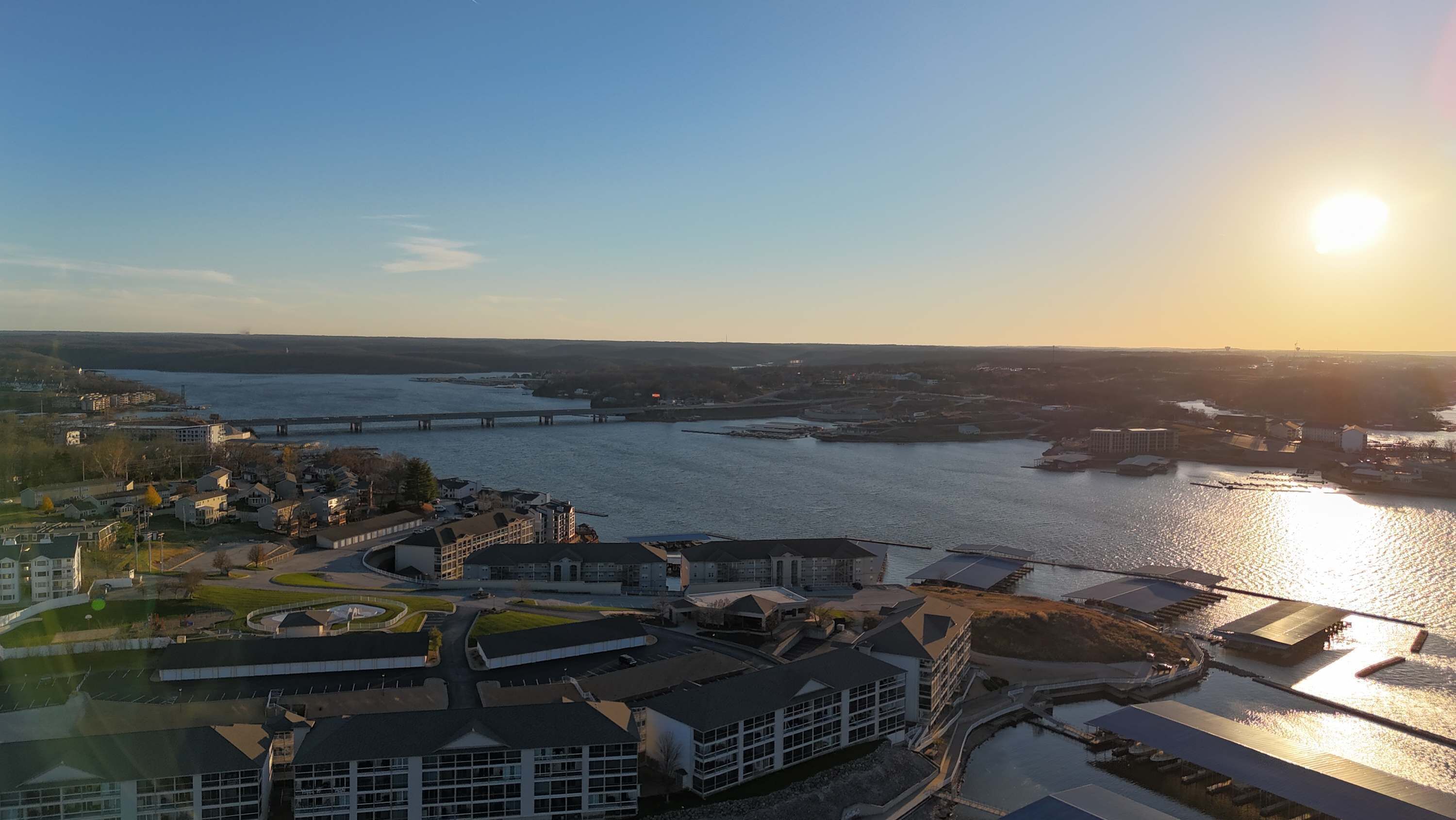A riverside view with buildings, a bridge, and a sun setting in the background.