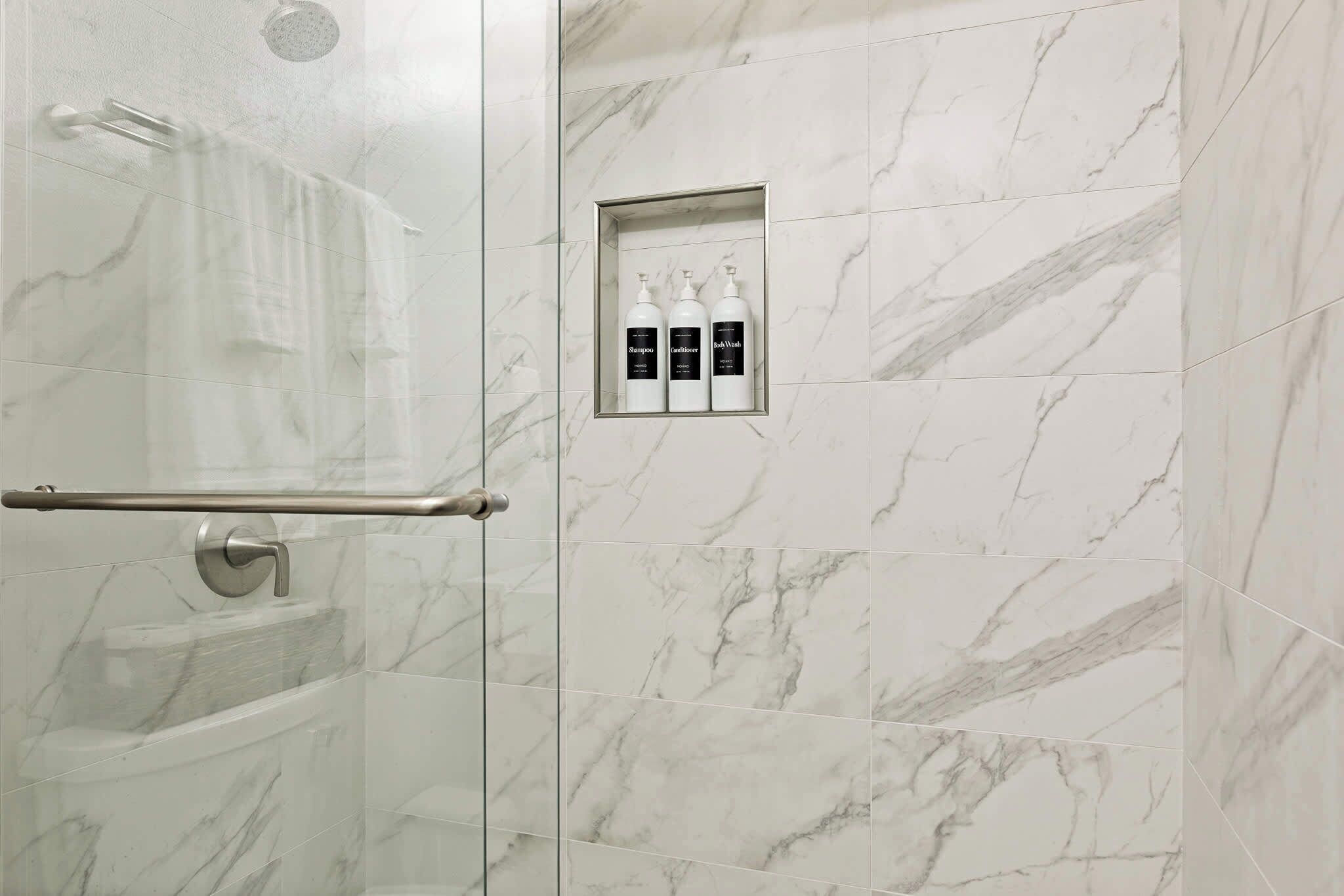 A bathroom with a glass shower enclosure, a towel rack, and a shelf with toiletries.