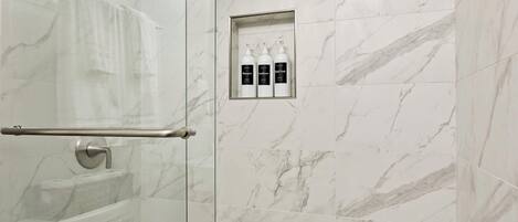 A bathroom with a glass shower enclosure, a towel rack, and a shelf with toiletries.