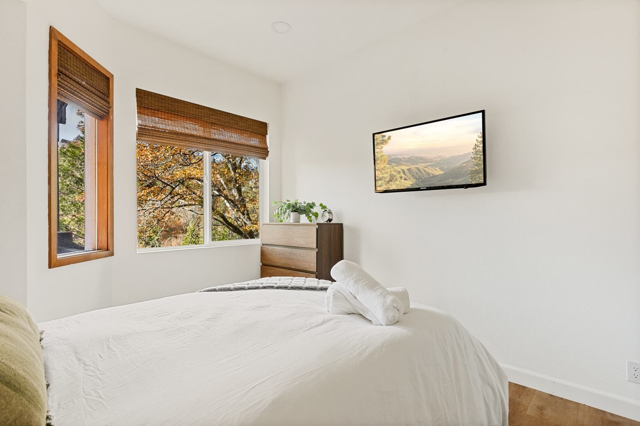 A bedroom with a bed, a dresser, a window with blinds, and a wall-mounted TV.