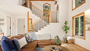 Un salon spacieux avec un canapé en cuir marron, une table basse ronde et un escalier doté de rampes en bois.