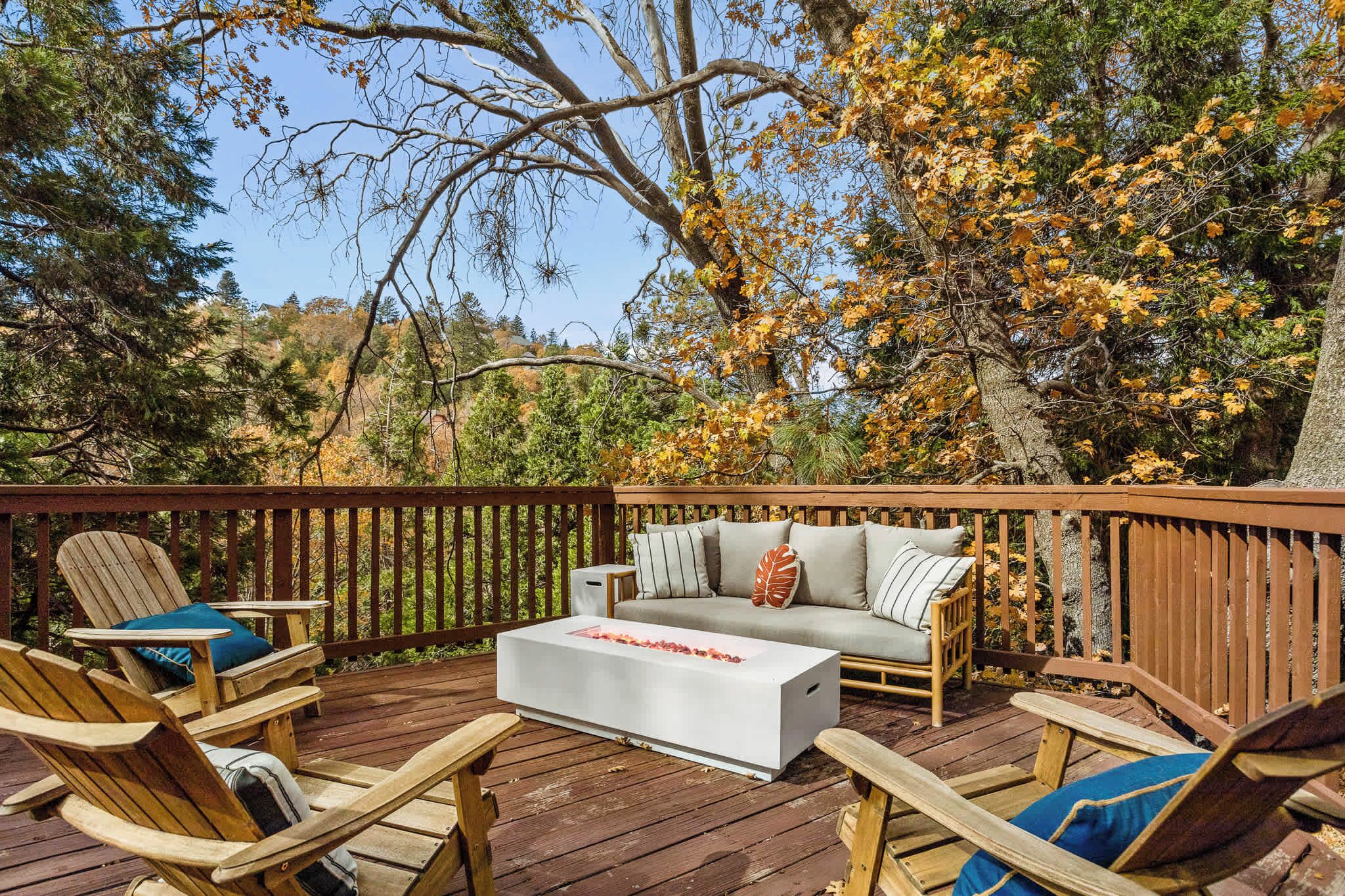 A wooden deck with outdoor furniture, including chairs and a sofa, surrounded by trees with autumn foliage.