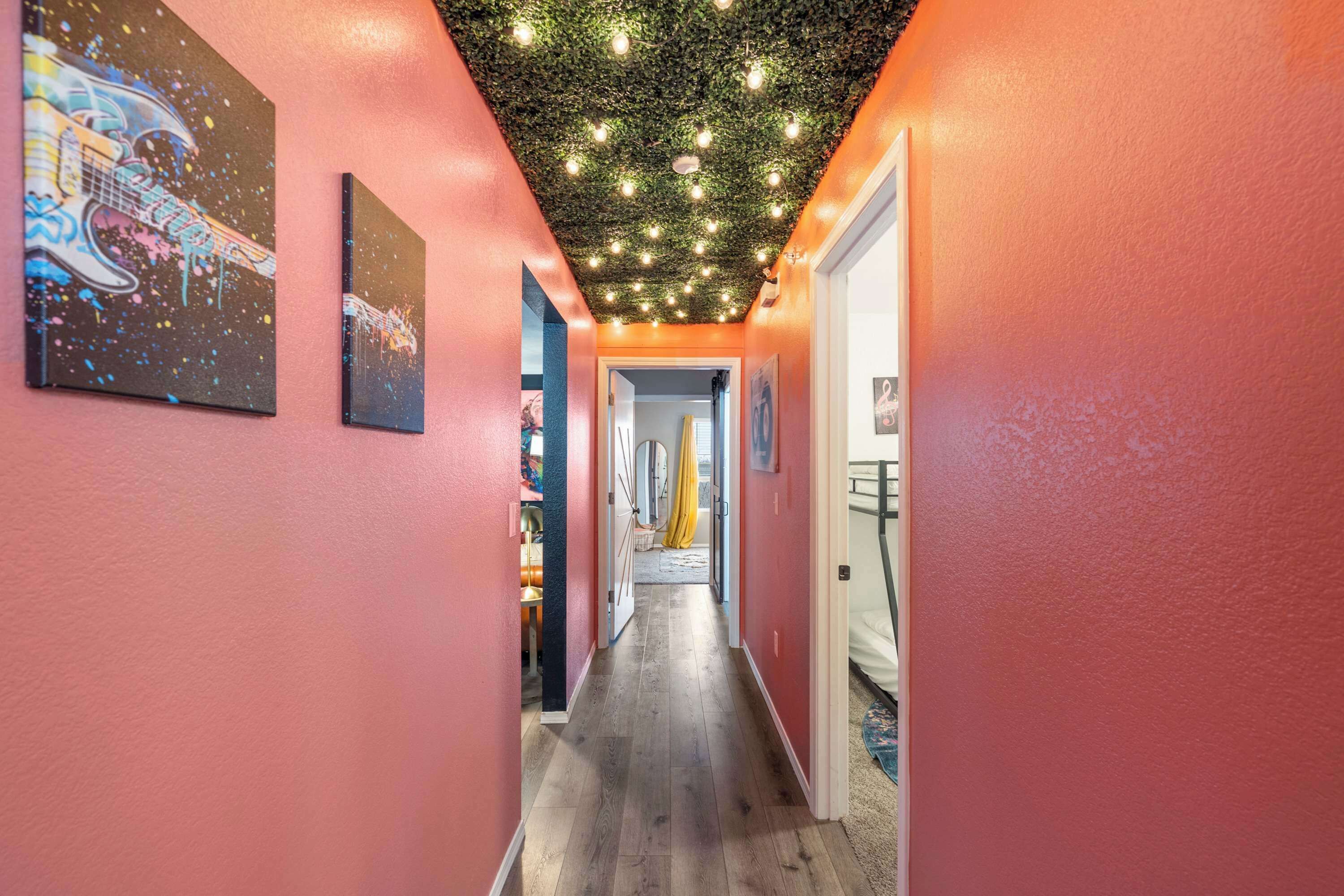 A hallway with pink walls, wooden flooring, and a ceiling with hanging lights.