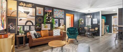 A modern living room with a brown leather sofa, a round wooden coffee table, and a teal armchair.