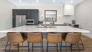 A modern kitchen with a large island, dark cabinets, stainless steel appliances, and four bar stools. - Big Bear Bungalow Stay on Ozark Waterfront (Gravois Mills)