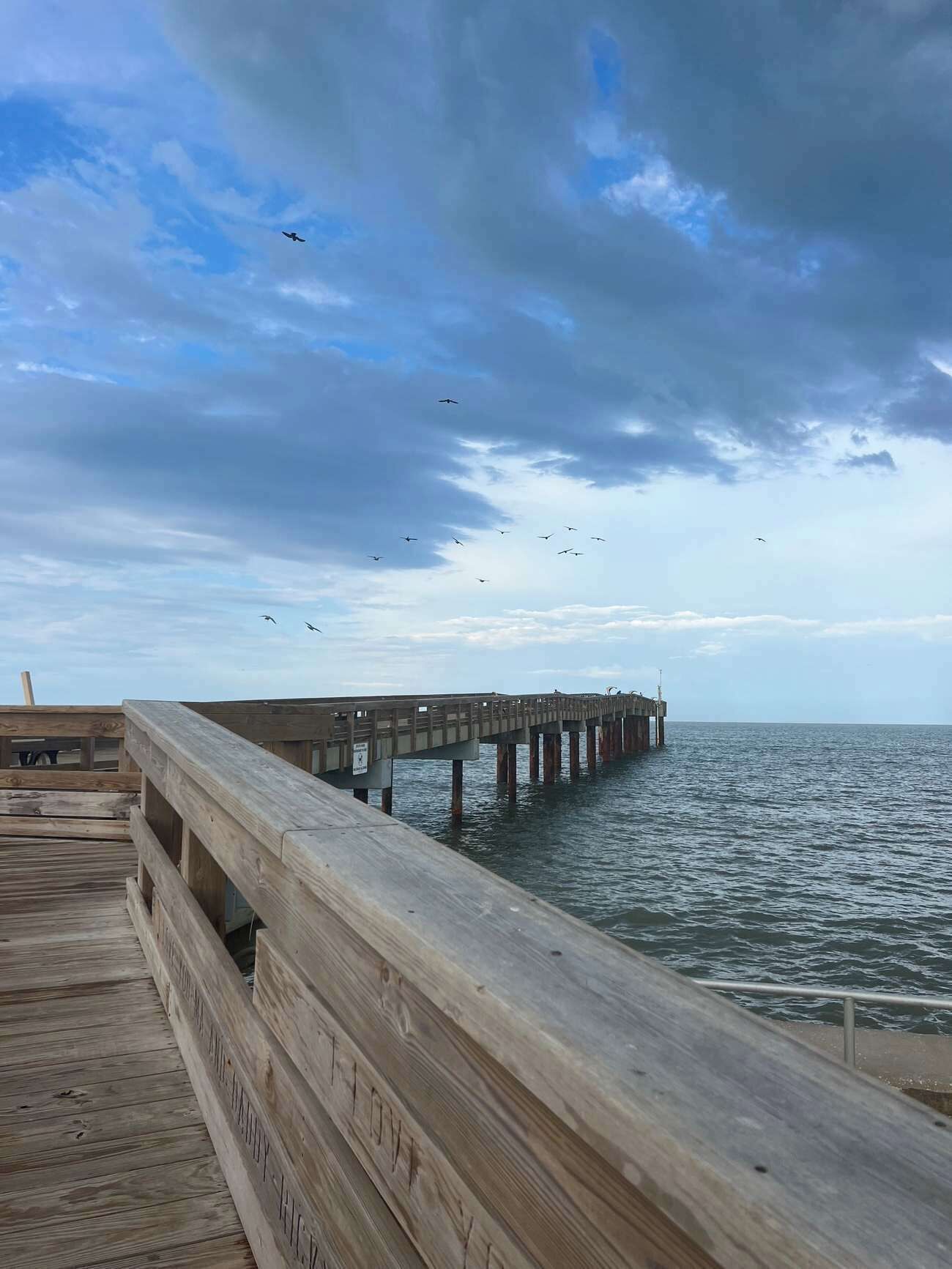 A wooden pier extending into a body of water with a cloudy sky above.