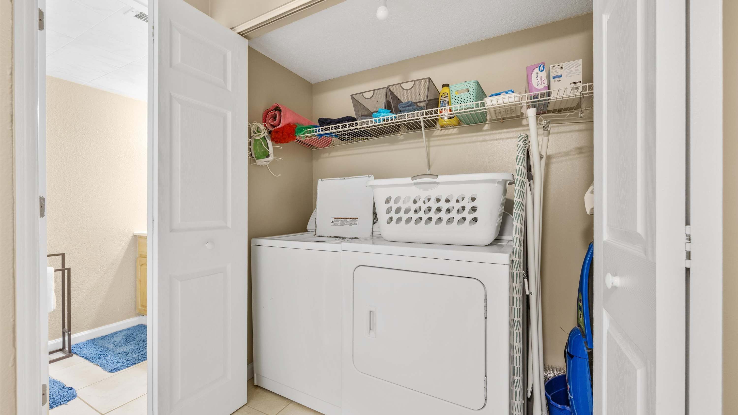 A laundry room with a washing machine, a drying rack, and a shelf with folded clothes and laundry supplies.
