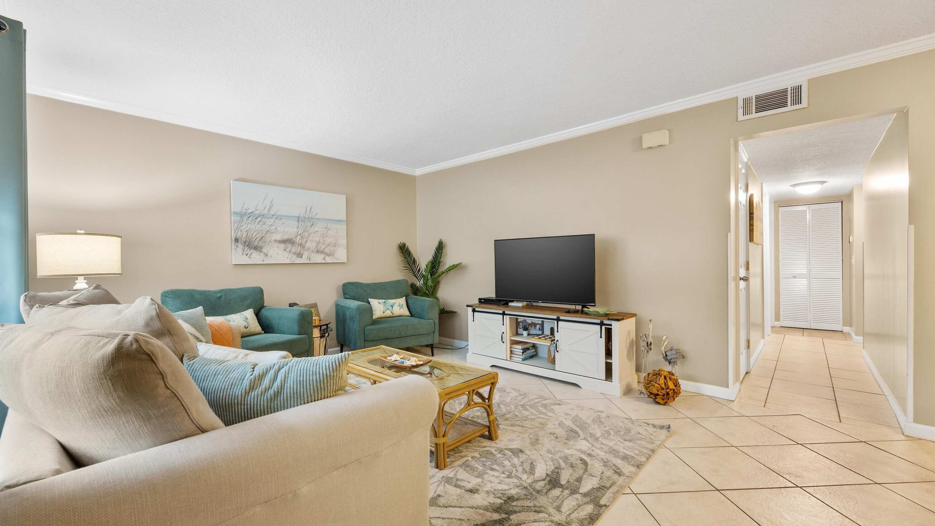 A living room with a sofa, two armchairs, a coffee table, a TV on a wooden cabinet, and a painting on the wall.