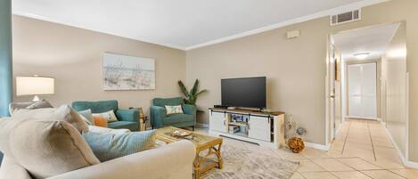 A living room with a sofa, two armchairs, a coffee table, a TV on a wooden cabinet, and a painting on the wall.