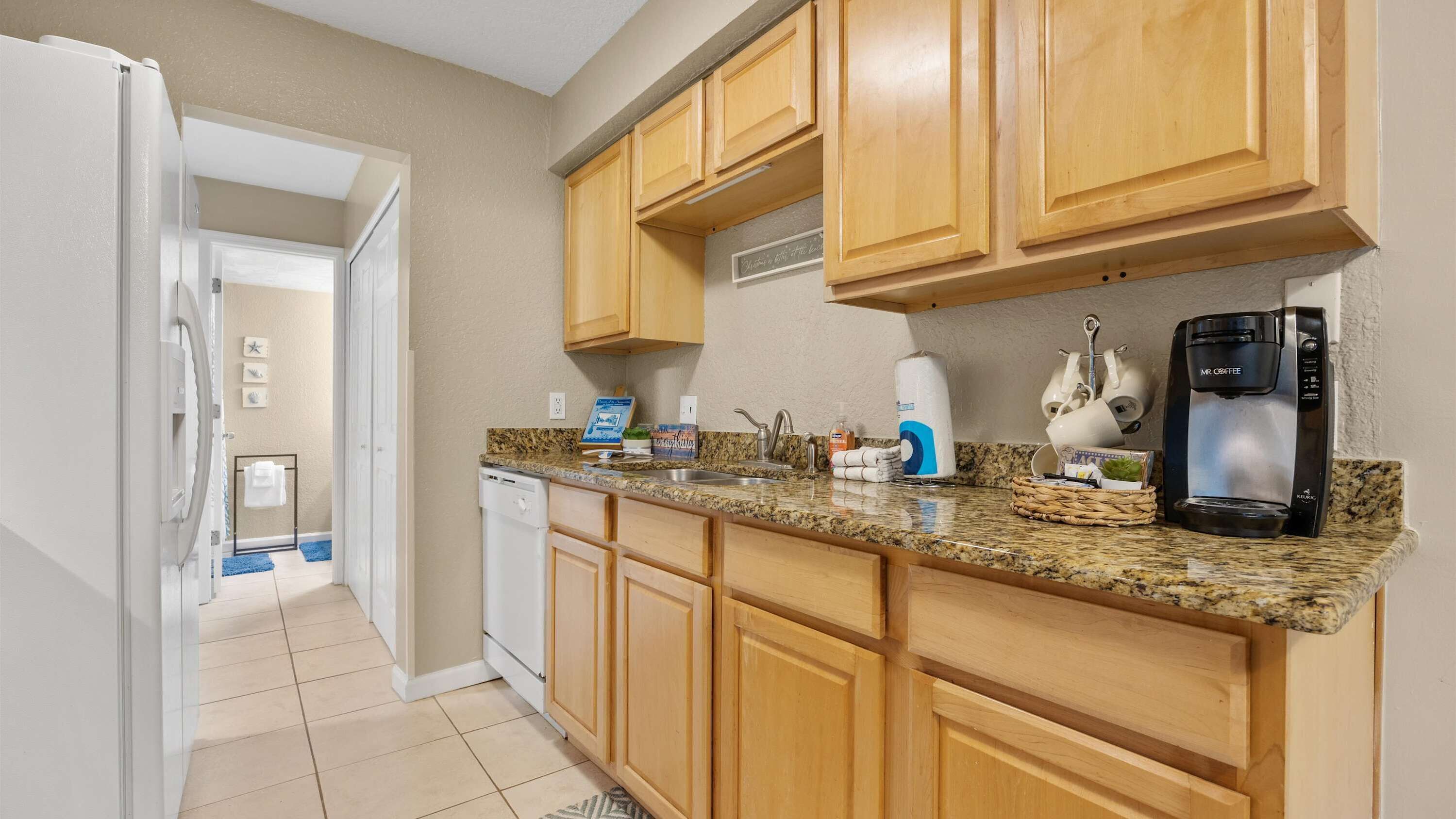 A kitchen with wooden cabinets, a granite countertop, a coffee maker, and a dishwasher.