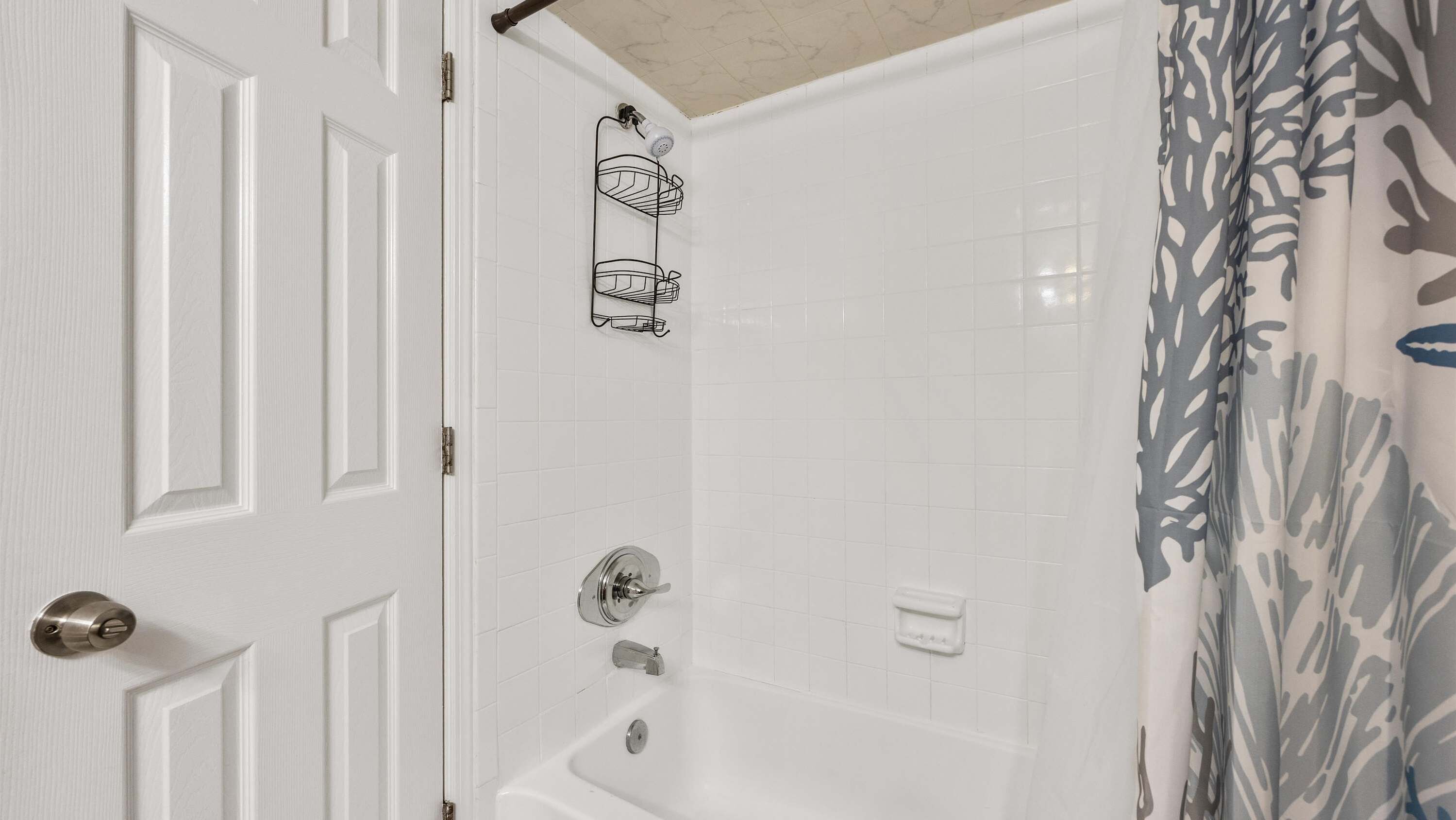 A bathroom with a white door, a shower with a shower curtain, and a bathtub.