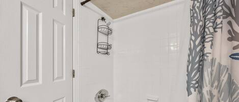 A bathroom with a white door, a shower with a shower curtain, and a bathtub.
