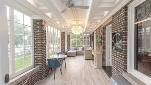 A sunlit room with a brick wall, a ceiling fan, a chandelier, and a large window. - Its Showtime Historic Downtown Geneva Escape! (Lake Geneva)
