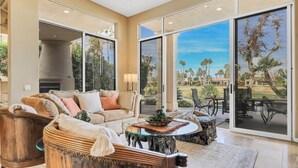 A spacious living room with a large glass door leading to a patio, a fireplace, and a view of a golf course.