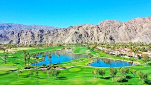 A golf course with multiple ponds and palm trees, surrounded by mountains and a residential area.