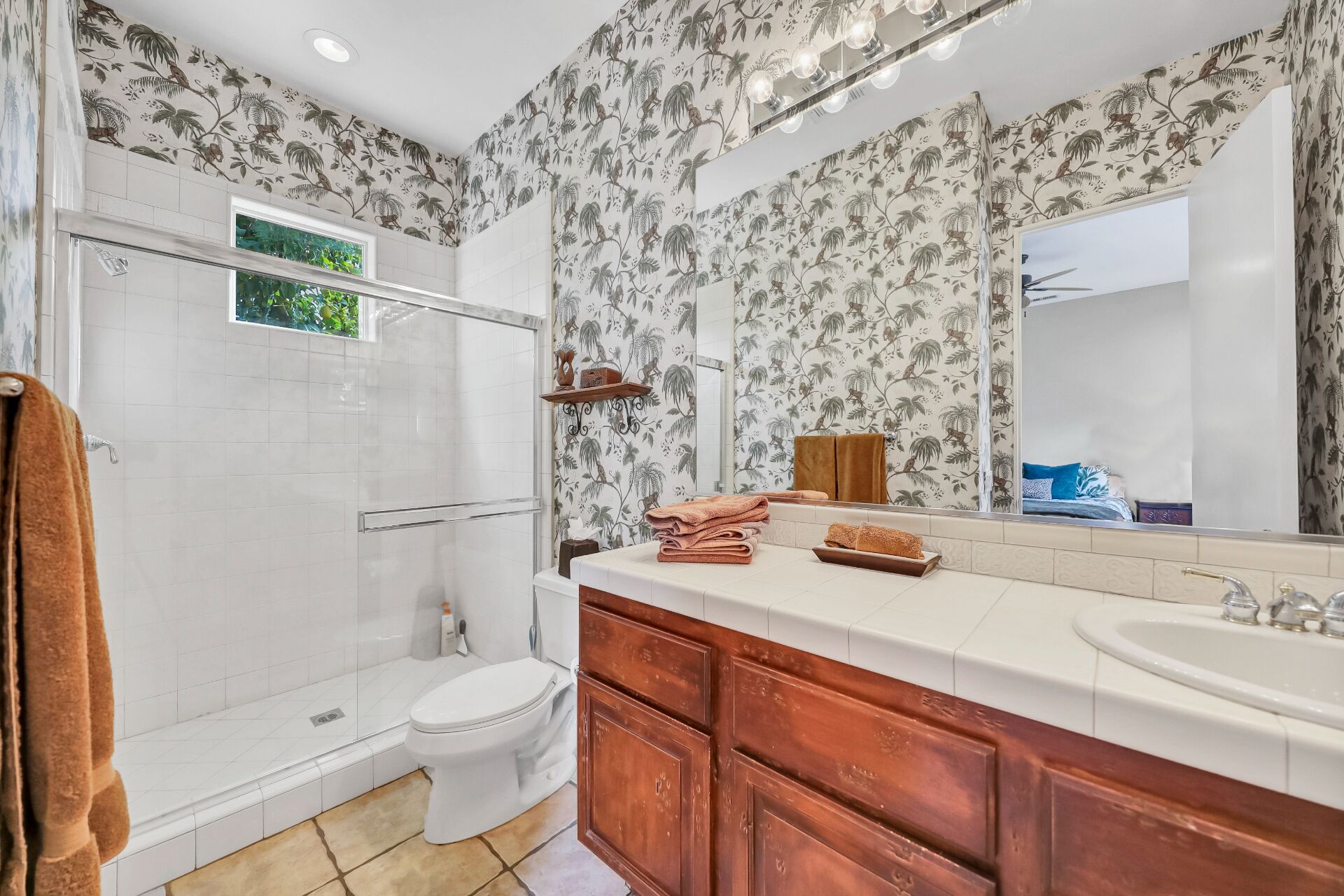A bathroom with a shower, toilet, vanity with a sink, and a large mirror.