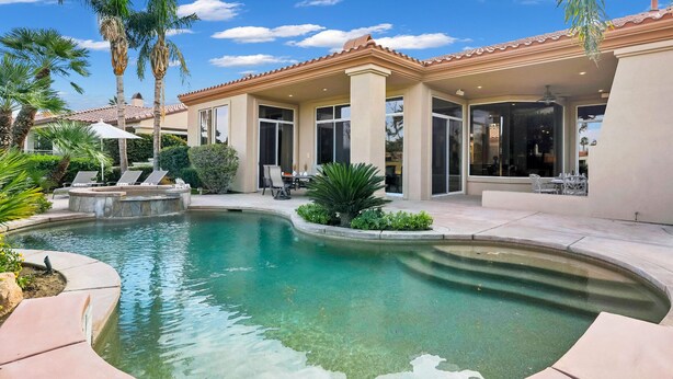 A pool area with a patio, palm trees, and a covered seating area.