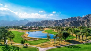 A golf course with a lake, palm trees, and mountains in the background.