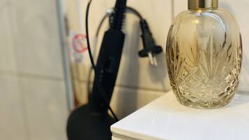 Een badkamer met een wit wastafelmeubel, een glazen fles met pompje en een zwarte haardroger op het aanrecht.
