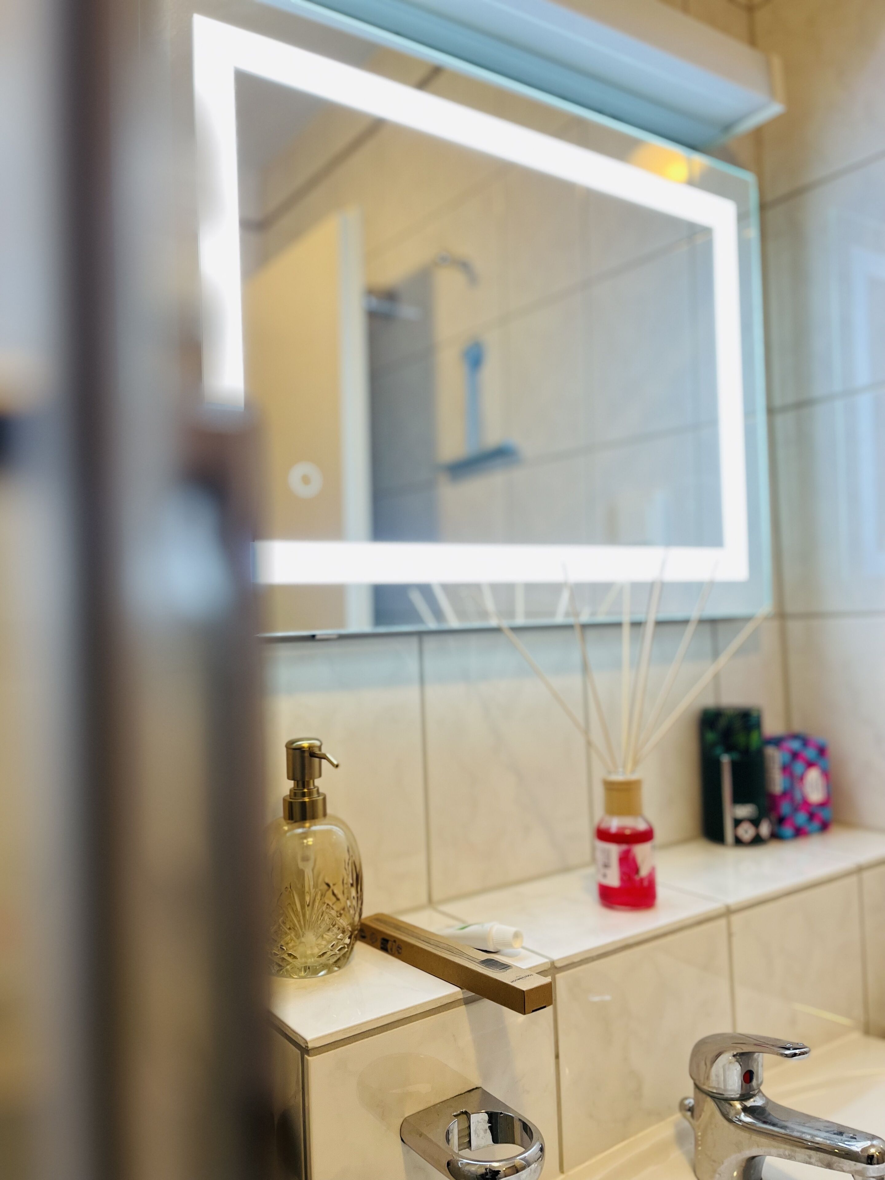 A bathroom with a mirror, a sink, a soap dispenser, and a bottle of hand sanitizer.