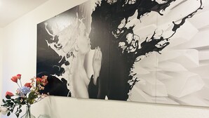 Un interior moderno con un cuadro abstracto grande, un florero de vidrio con flores y una consola negra.