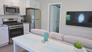 A modern kitchen with white cabinets, stainless steel appliances, and a flat-screen TV mounted on the wall.
