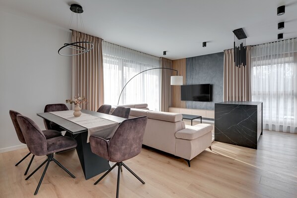 Un salon moderne comprenant un coin repas, un canapé, un téléviseur et une table d’appoint en marbre.