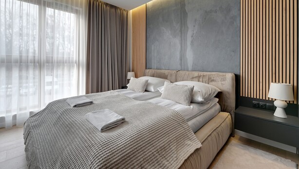 Un dormitorio moderno con una cama grande, una mesita de noche con lámpara y vistas a árboles a través de cortinas traslúcidas.