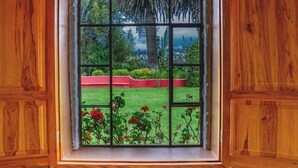 Una ventana con vistas a un jardín, que incluye césped, macizos de flores rojas y árboles.