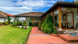 Una casa tradicional con tejado de baldosas, un jardín con diversas plantas y un cielo azul despejado.