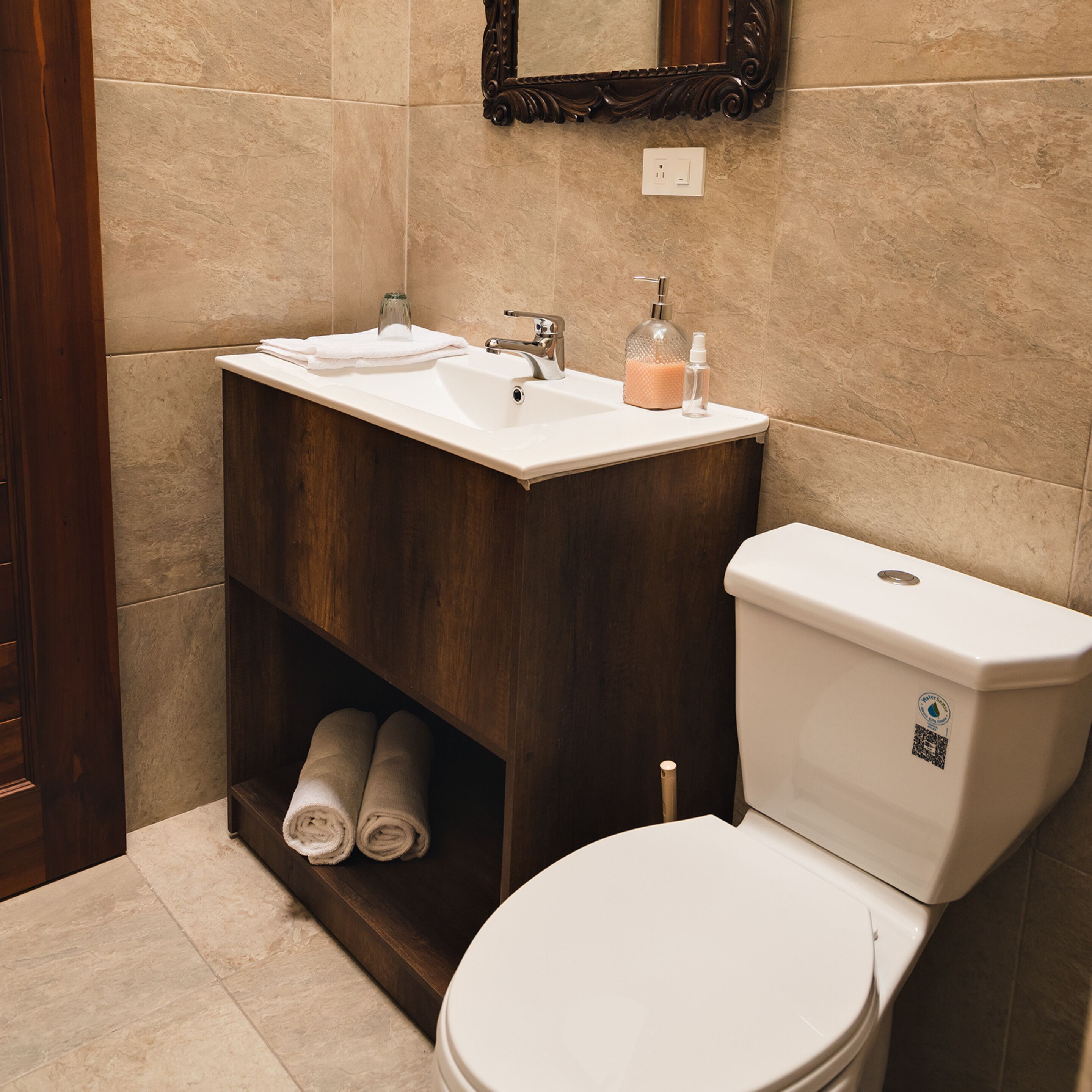 A bathroom with a white sink, dark wooden vanity, a toilet, and a mirror above the sink.