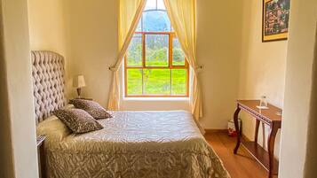 A bedroom with a large window, a bed with a headboard, a bedside table, and a small table with a glass.