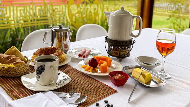 Una mesa de desayuno con café, pasteles, fruta y un vaso de jugo.